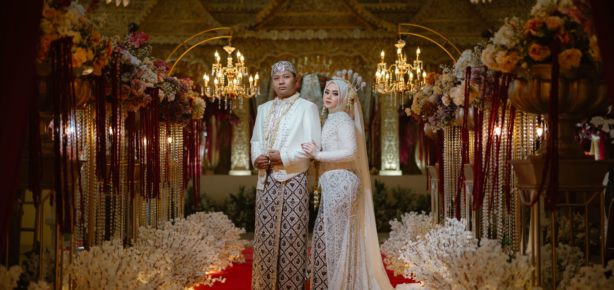 Pasangan pengantin berbusana adat Jawa di pelaminan bernuansa emas